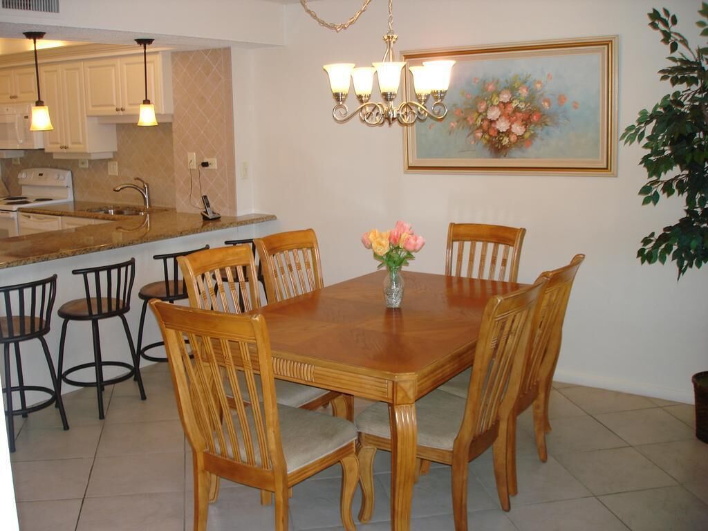 A dining area with a wooden table and chairs, a vase with flowers, a chandelier, and a painting on the wall.