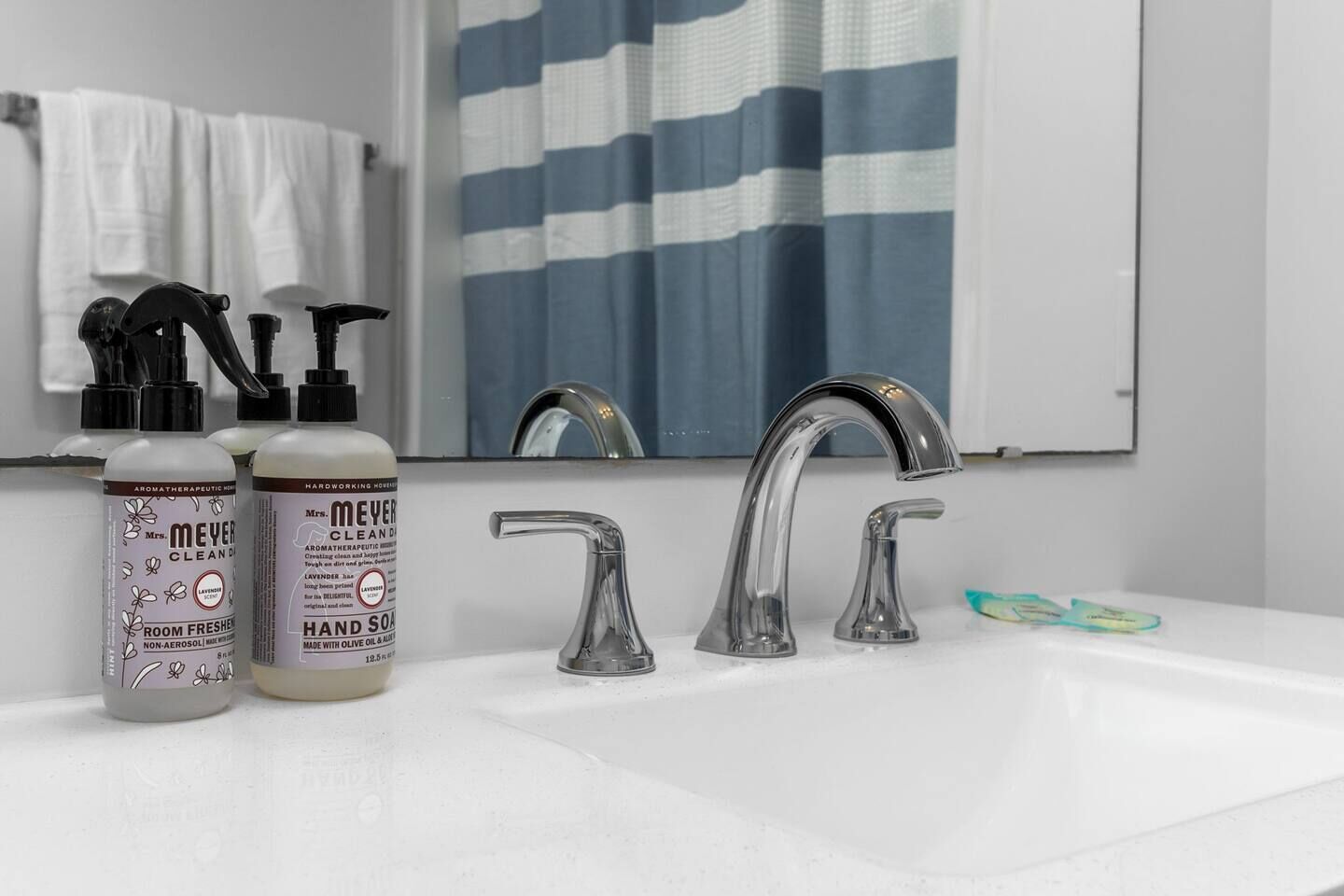 A bathroom with a white sink, two bottles of hand soap, a faucet, and a striped shower curtain.