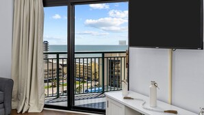 Un balcon avec vue sur la mer et les bâtiments, une table de chevet blanche et un rideau.