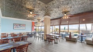Un restaurant spacieux avec de hauts plafonds, des motifs décoratifs élaborés et de grandes fenêtres offrant une vue sur la plage.
