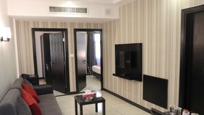 Ein modernes Hotelzimmer mit einer Couch, einem Couchtisch, einem an der Wand montierten Fernseher und einer Tür zum Schlafzimmer.