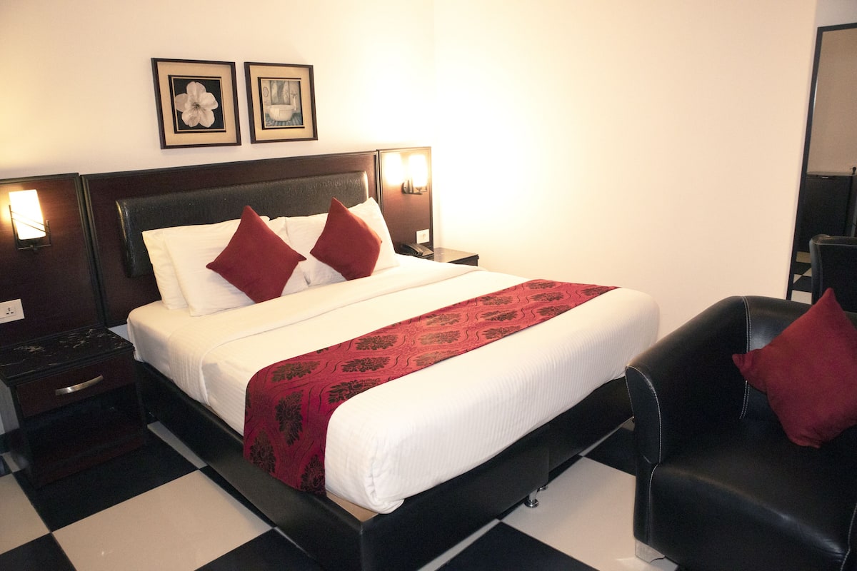 A hotel room with a bed, a nightstand, a chair, and two wall-mounted lamps.