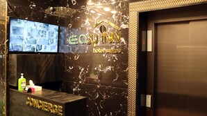 Ein Empfangsbereich mit digitalem Bildschirm, der mehrere Kameraansichten zeigt, ein Concierge-Bereich und eine Marmorwand mit dem Hotelnamen.