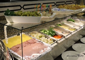 A buffet with various food options including sliced meats, vegetables, and a bowl of olives.