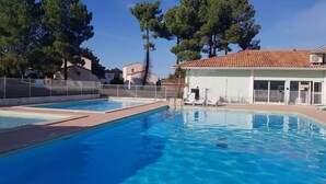 Une piscine de deux couloirs, entourée d’une clôture blanche et jouxtant un bâtiment dont le toit est recouvert de tuiles.