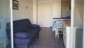 Un espace de vie compact comprenant un canapé, une table à manger avec des chaises, un coin cuisine et une porte donnant sur une autre pièce.