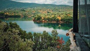 Une vue sur le lac, avec une terrasse en bois donnant sur un lac paisible, le tout entouré d’une végétation luxuriante et de collines.