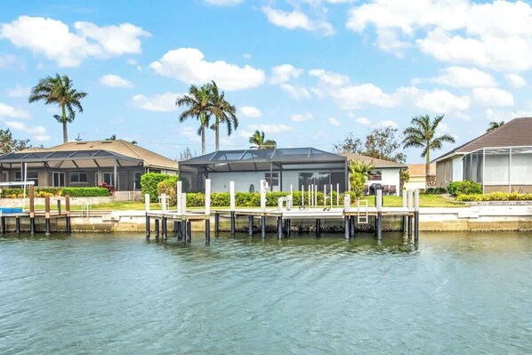 A waterfront property with a dock extending into a body of water, surrounded by palm trees and modern buildings. - Walking Distance to the Beach! Canal / Pool Home! (Marco Island)