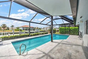 A swimming pool with a covered area, clear skies, and a view of surrounding buildings. - Walking Distance to the Beach! Canal / Pool Home! (Marco Island)