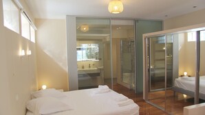 A modern hotel room with a bed, a bathroom with a glass shower, and a sliding glass door leading to a balcony.