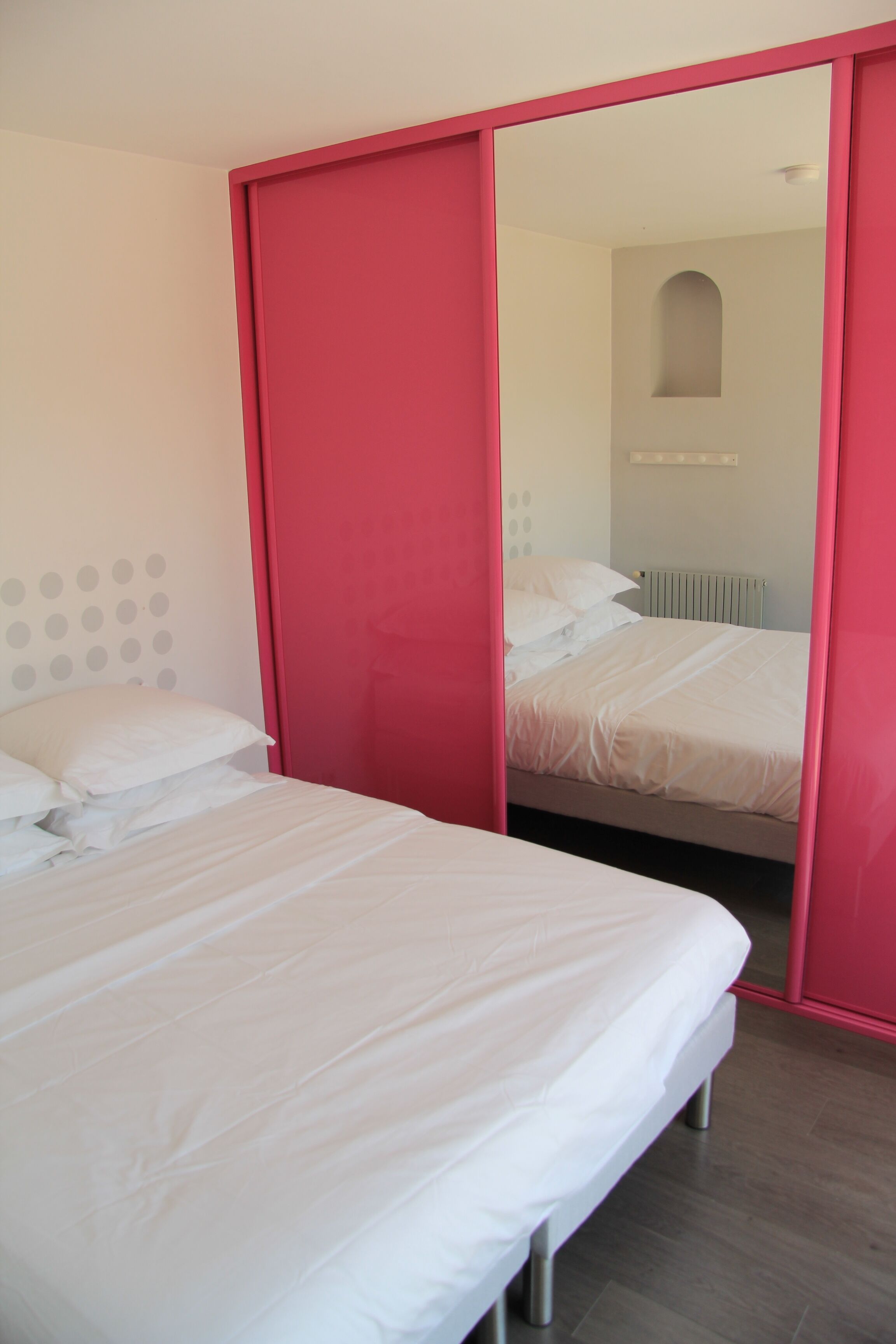A bedroom with a bed, a red wardrobe, and a mirrored closet door.