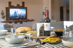 A dining table with a bottle of wine, bowls, plates, and a television in the background.