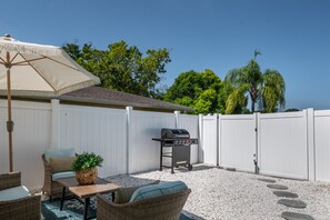 Un patio trasero con una parrilla, muebles de mimbre y una cerca blanca.