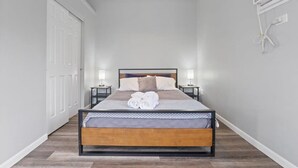 Una habitación estrecha y bien iluminada con una cama individual, lámparas de noche y un aire acondicionado instalado en la pared.