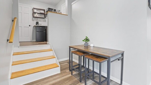 Una escalera conduce a una zona de cocina con una mesa de madera y taburetes de bar.