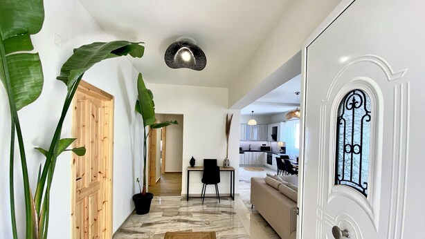 A hallway with a wooden door, a potted plant, a rug, a dining area, and a kitchen. - Ionia's apartment,3 bedrooms,Next to all amenities (Missiria)