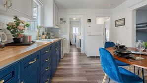 Moderni keittiö, jossa on puinen työtaso, siniset kaapit ja ruokailutila, jossa on pöytä kahdelle.
