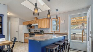 A modern kitchen with wooden cabinets, a central island with stools, and pendant lighting. - Mountain Time | Furnished 30+ Day Retreat (Crowsnest Pass)