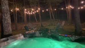 Un área de hidromasaje al aire libre con luces colgantes, rodeada de árboles y sillas.