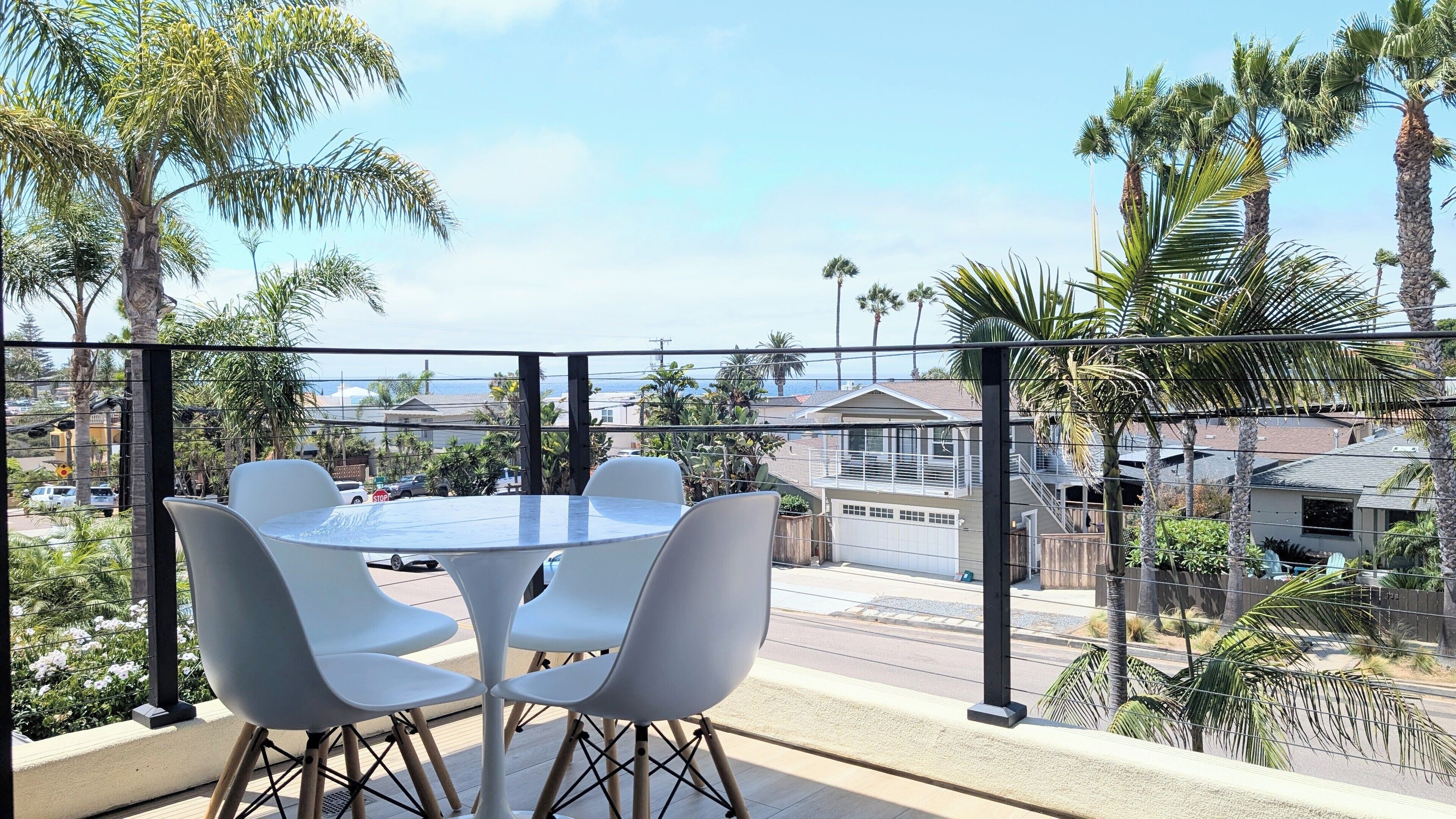 Een balkon met een tafel en stoelen, met uitzicht op een woonwijk met palmbomen en huizen.