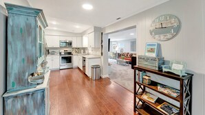 A modern kitchen with white cabinets, a wooden floor, and a blue vintage-style clock on the wall.