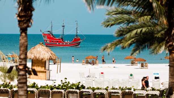 A beach with a red boat, lounge chairs, and umbrellas.