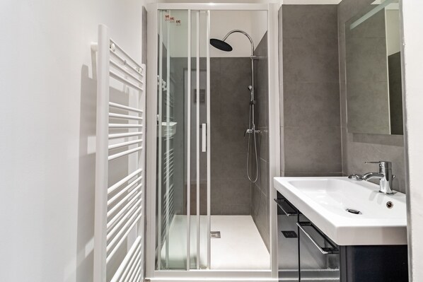 Une salle de bain moderne avec une douche à parois de verre, un lavabo blanc et un grand miroir.