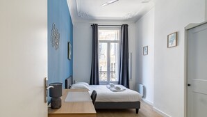 A bedroom with a bed, a desk, and a window with curtains.