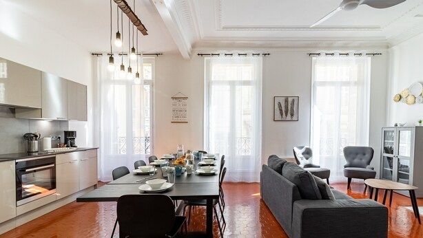 A modern kitchen with a dining area, a gray sofa, and a small table.