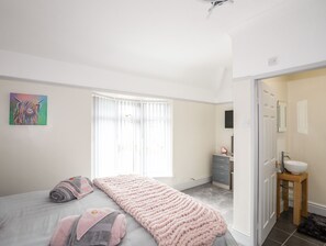 A bedroom with a bed, a bedside table, a dresser, and a window with blinds.