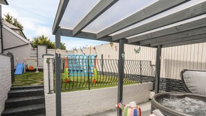 Ein überdachter Außenbereich mit Whirlpool, Spielgerüst und einer Treppe, die zu einem Haus führt.