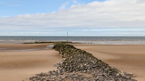 Ein sandiger Strand mit einem steinernen Wellenbrecher, der sich ins Meer erstreckt.