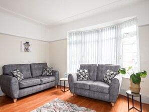 A living room with two grey sofas, patterned cushions, a small round table, and a potted plant.
