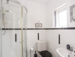 A modern bathroom with a glass shower enclosure, a toilet, a sink, and a window providing natural light.