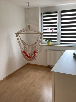 A room with a hanging hammock chair, a window with blinds, a radiator, and a white table. - Vacation apartment in the border triangle, 3 rooms 64 sqm, fully equipped. 1ST FLOOR (Steinen)