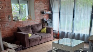 Un salon avec un mur en briques, un canapé marron, une table basse en verre et une petite table ronde.