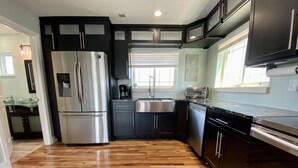 Une cuisine moderne avec des meubles de couleur sombre, des appareils électroménagers en acier inoxydable et un plancher en bois.