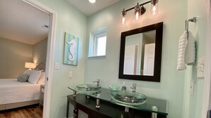 Une salle de bain moderne avec un lavabo en verre, des meubles sombres, un grand miroir et une œuvre d’art représentant un hippocampe.
