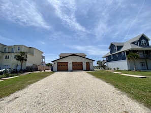A residential street with a gravel driveway leading to a house with two garage doors.