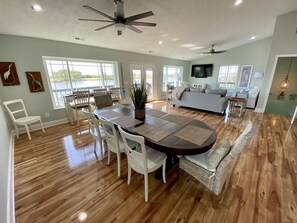 A spacious living room with a large dining table, white chairs, and a grey sofa.
