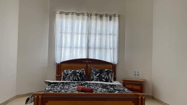 A bedroom with a wooden bed, a nightstand, a small table, and a window with curtains.