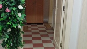 A hallway with a checkered floor, a potted plant with flowers, a wooden wardrobe, and a door with a 'home' mat.