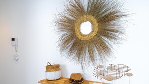 Un espejo montado en la pared con diseño de sol, una cesta trenzada, un sombrero y una escultura de pez sobre un estante de madera.