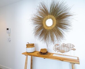 Un miroir mural orné d’un motif en forme de soleil, un panier tressé, un chapeau et une sculpture de poisson, le tout posé sur une étagère en bois.