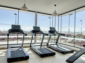 Une salle de sport équipée de tapis de course et d’un banc, avec de grandes fenêtres et une vue sur l’extérieur.