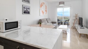 Une cuisine moderne dotée d’un four à micro-ondes encastré, un coin repas avec une table et des chaises, un canapé gris et un balcon avec vue.