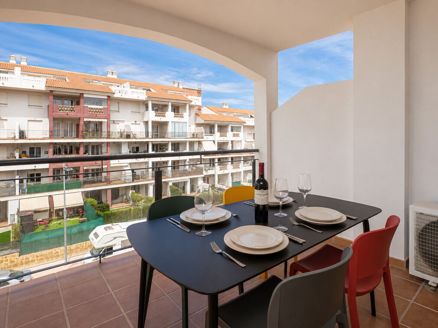 A balcony with a table set for two, overlooking a residential area with multiple buildings.