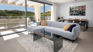 Ein modernes Wohnzimmer mit einem Glastisch, einem grauen Sofa und einem Essbereich mit Tisch und Stühlen.