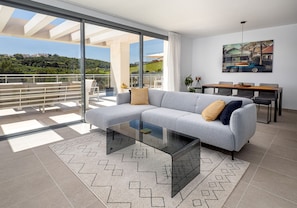 A modern living room with a glass coffee table, grey sofa, and a dining area with a table and chairs. - Casares Green 2365 Golf & Luxury (Casares)
