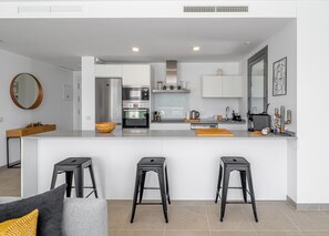 A modern kitchen with a central island, bar stools, and a dining area with a sofa. - Casares Green 2365 Golf & Luxury (Casares)